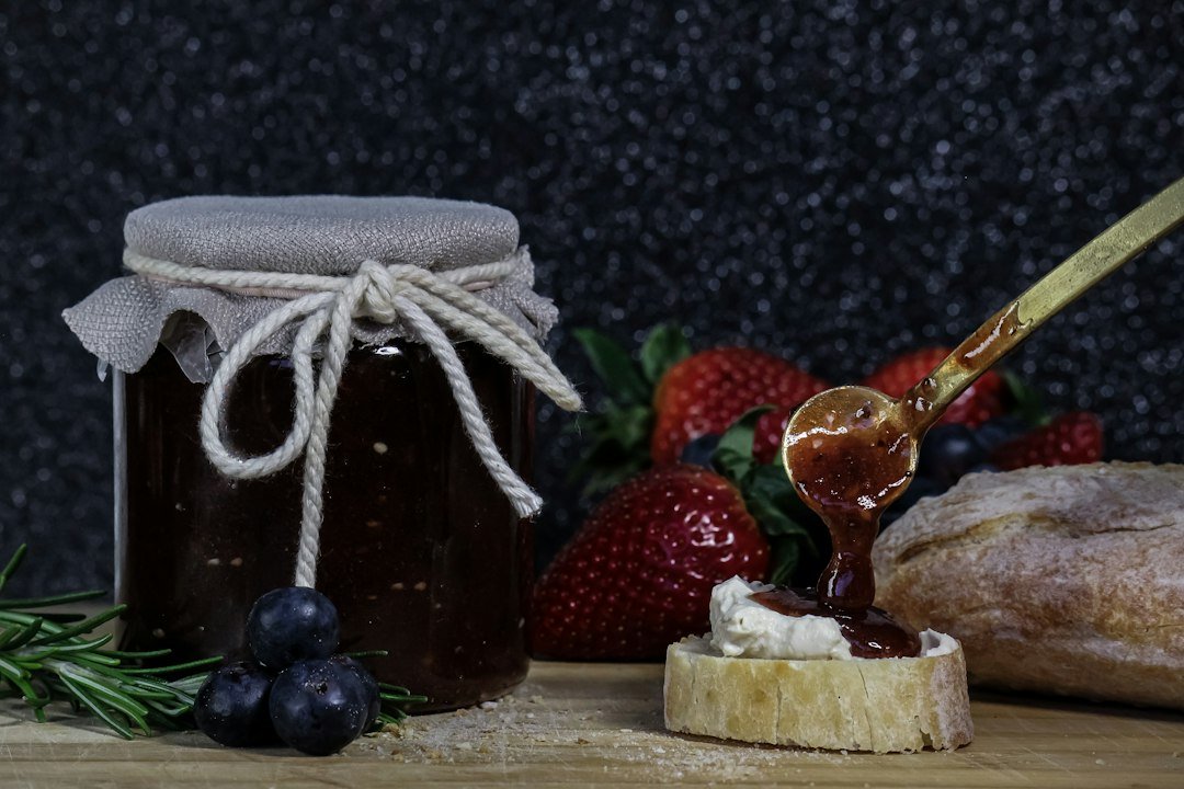 Glass jar of homemade berry jam with a spoon and fresh berries