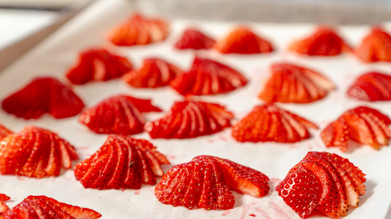 Fresh strawberry slices arranged in a single layer on a baking tray before freezing to keep berries separate